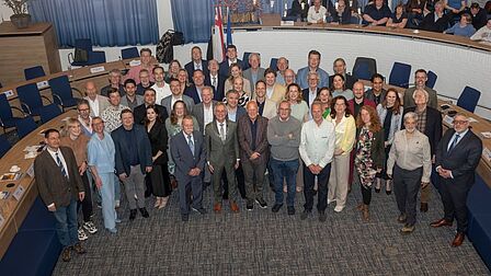 Foto van een grote groep mensen in een raadzaal