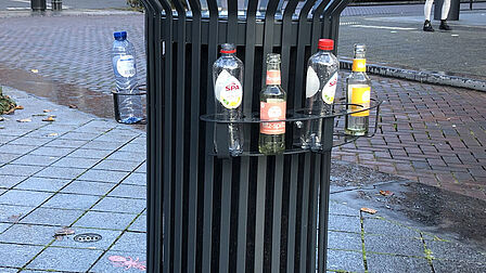 Foto van een openbare vuilnisbak met een metalen ring eromheen waar statiegeldflesjes staan.