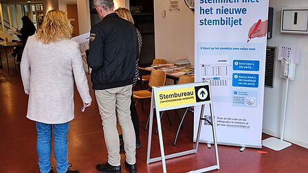Foto van mensen in een stembureau met uitleg over het nieuwe stembiljet.