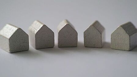 Foto van vijf kleine grijze houten huisjes tegen ene grijze achtergrond.
