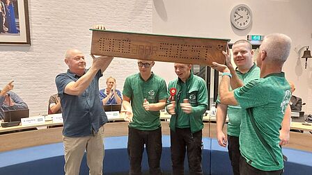 Foto van vijf mensen die een houten voorwerp met '100 jaar Soest' omhoog houden in de raadzaal.